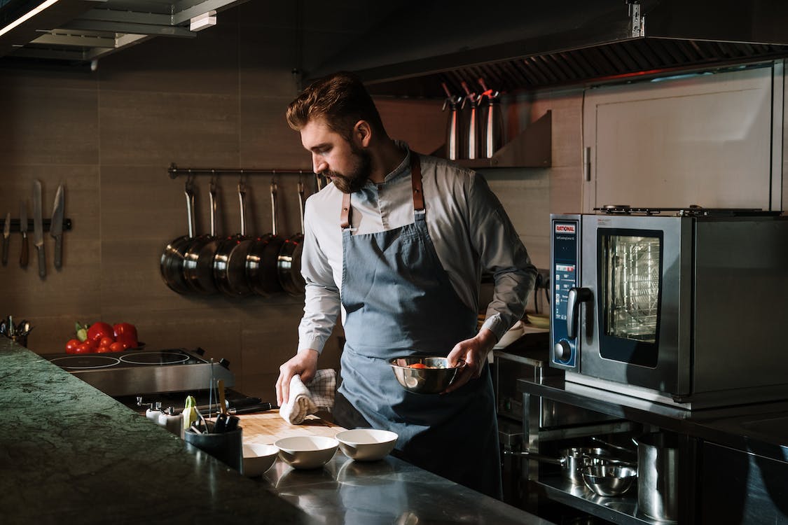 chef holding a silver bowl of food in the kitchen