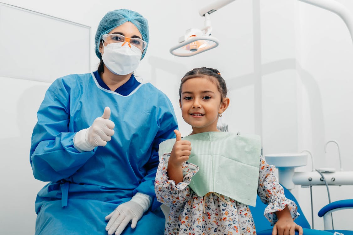 dentist in scrubs doing a thumbs up with child patient