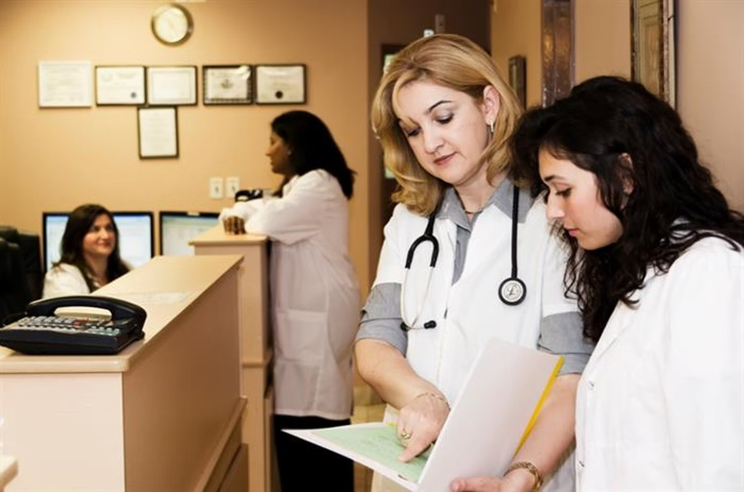 two doctors in a doctors waiting room discussing something on a clipboard
