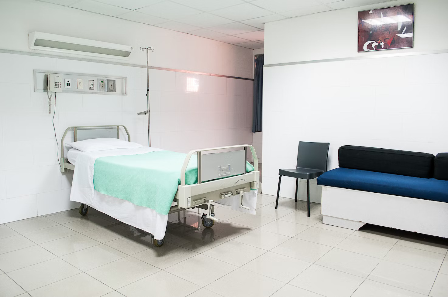 white hospital room with a hospital bed and sofa in the corner
