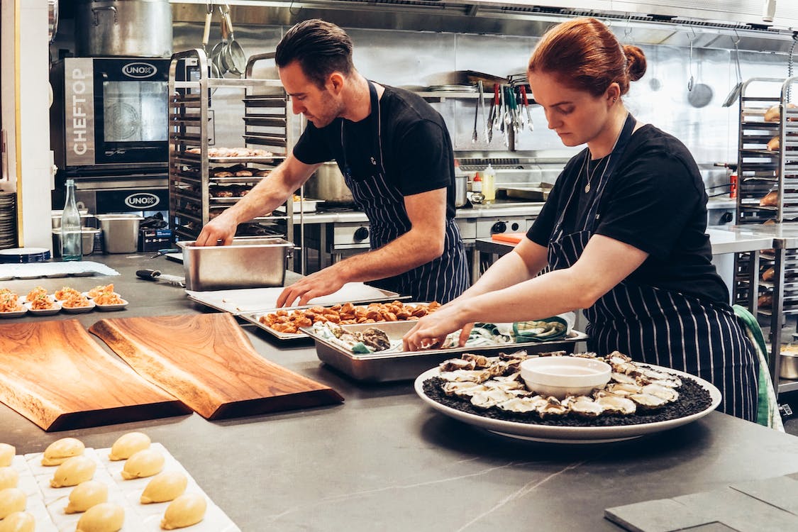 two chefs  prepping seafood on top of a stone kitchen countertop in an industrial kitchen.