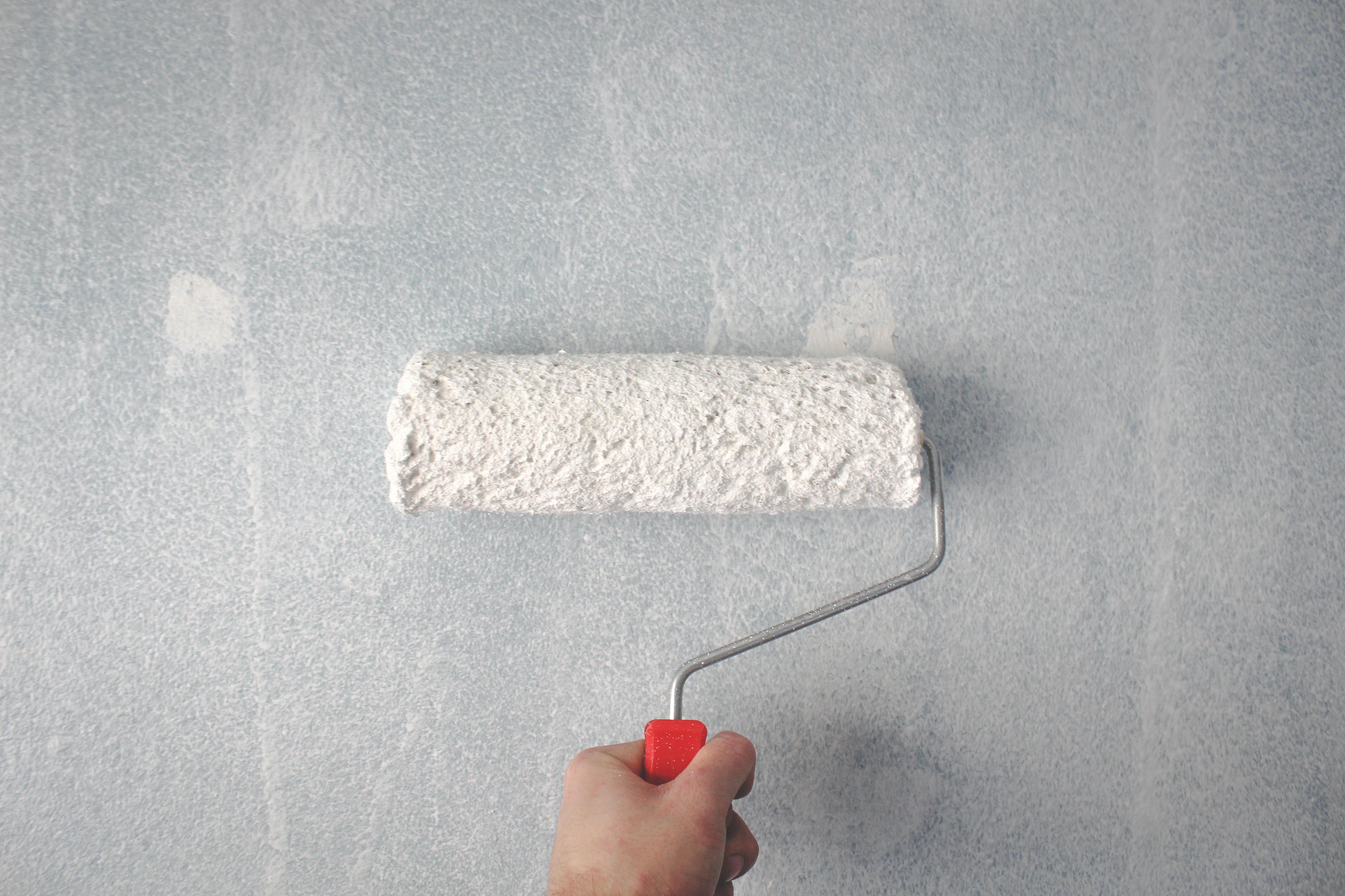 Hand rolling white paint onto a wall using a paint roller