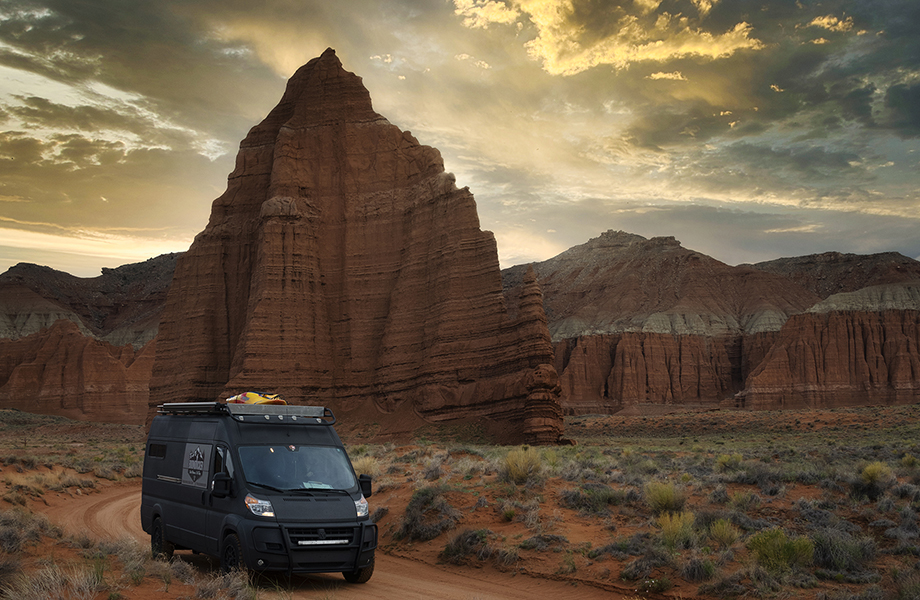 Camper van driving on a dirt road with a mountain peak in the background